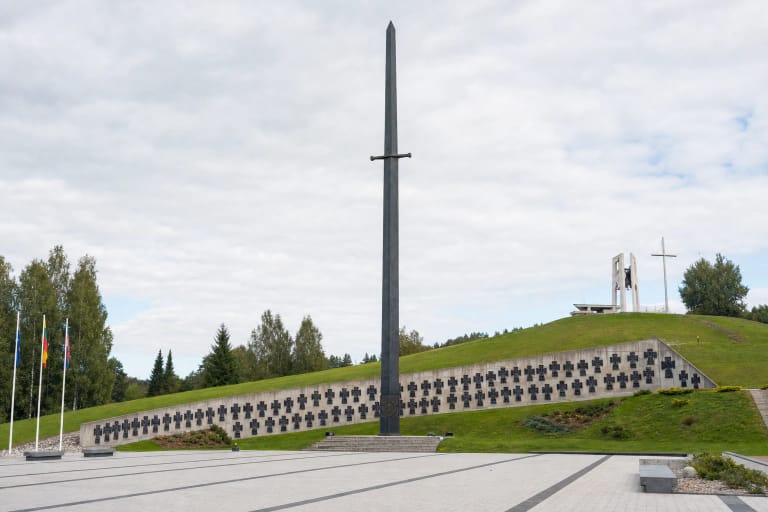 Kryžkalnio partizanų memorialo kalavijo formos obeliskas, vardų siena ir akmenimis grįsta ceremonijų aikštė žaliame šlaite