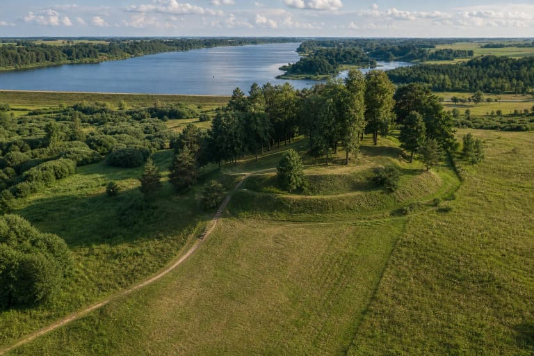 Зелёное кольцо земляных укреплений и деревья на вершине городища Купишкис (Аукштупенай), вдали Купишкисское водохранилище