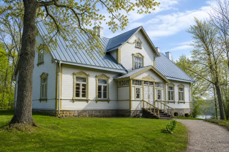 Kuršėnų etninės kultūros ir tradicinių amatų centro baltas medinis pastatas su puošniais langų apvadais ir parku