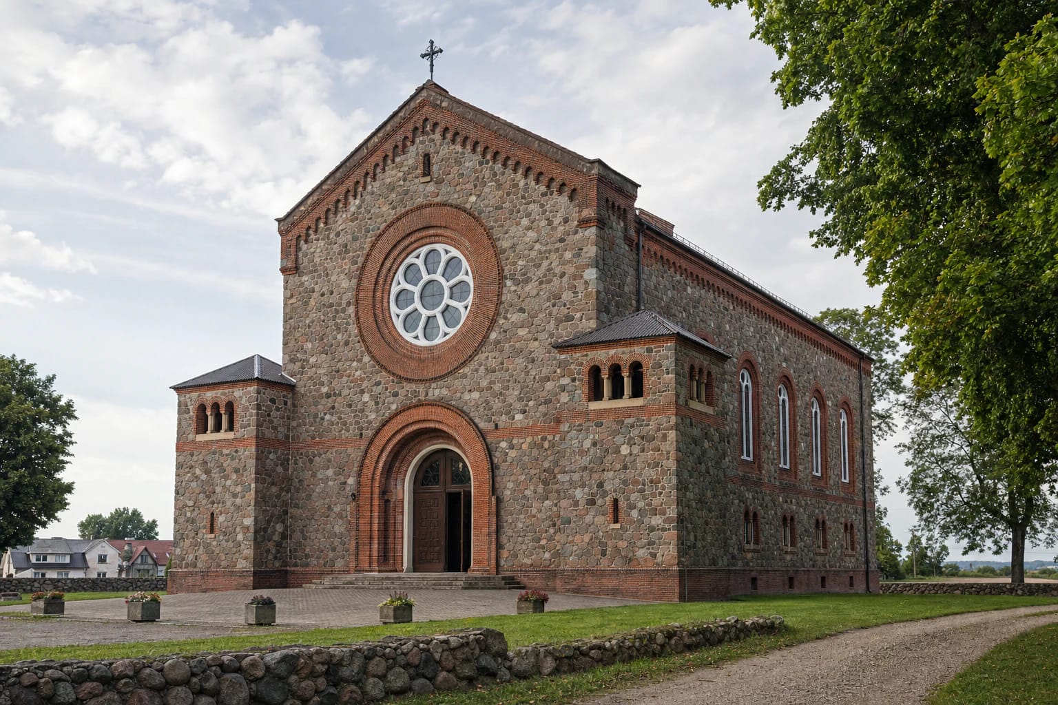Fieldstone and red-brick façade of Kvėdarna Church with a large rose window, arched entrance, and low side turrets