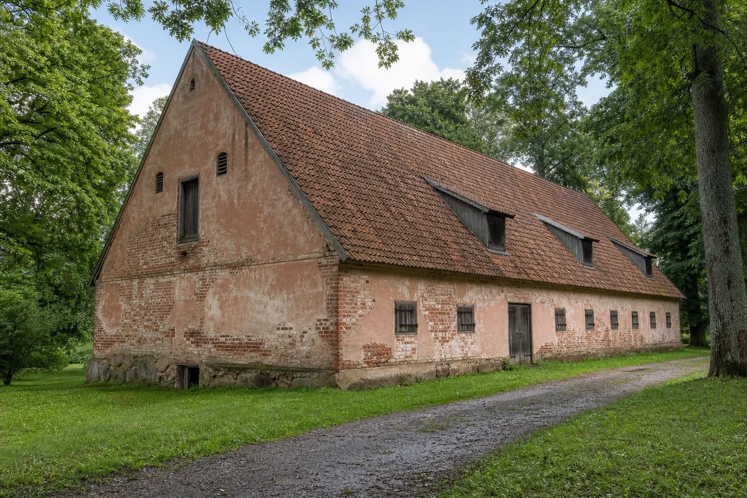 Nineteenth-century masonry warehouse at Kvietiškis Manor Estate, with a steep tiled roof and small dormers among mature park trees