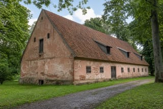 Nineteenth-century masonry warehouse at Kvietiškis Manor Estate, with a steep tiled roof and small dormers among mature park trees