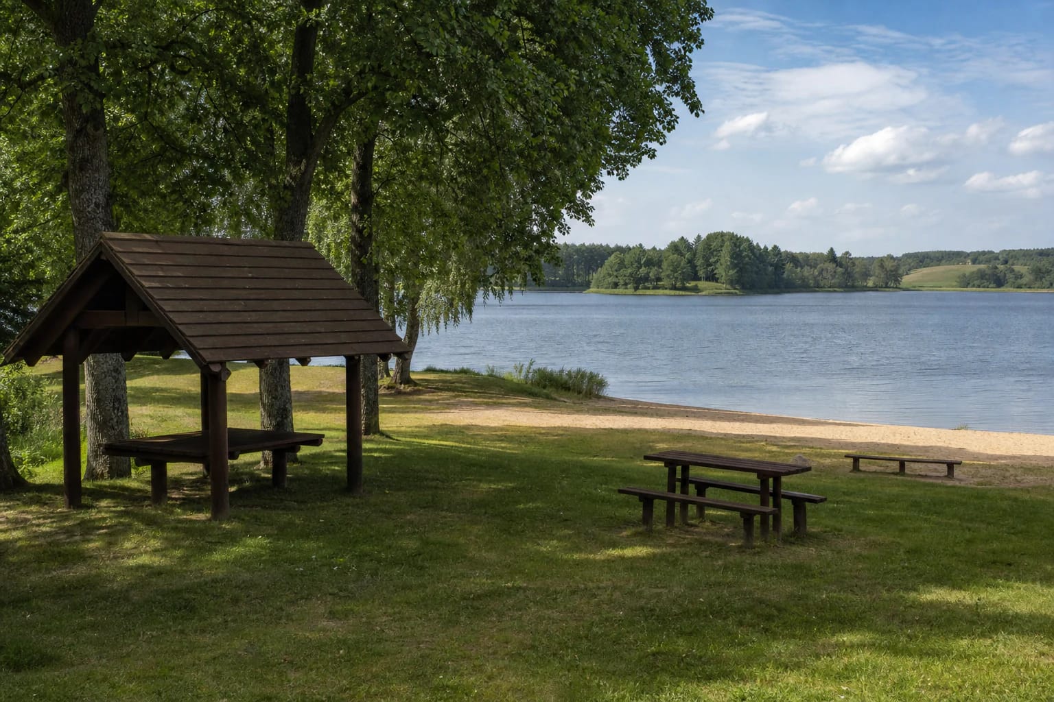Laičiai II (Paežeriai) Dam Bathing Site with a sandy shore, green lawn, wooden shelter, and calm water