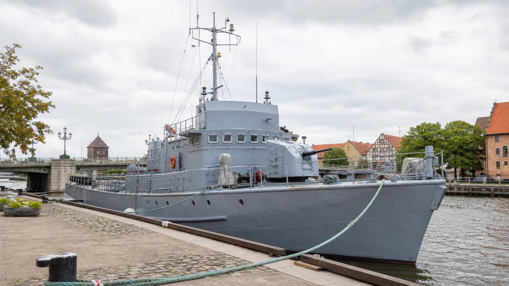 Ship-Museum Sūduvis by the Danė quay in Klaipėda, with a grey naval hull, deck, and Pilies Bridge surroundings