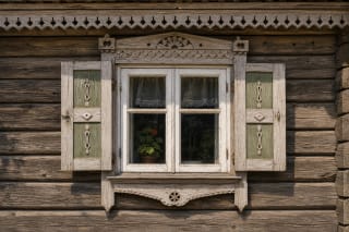 A wooden Lithuanian house window with painted shutters, white trim, an openwork upper trim, and floral motifs