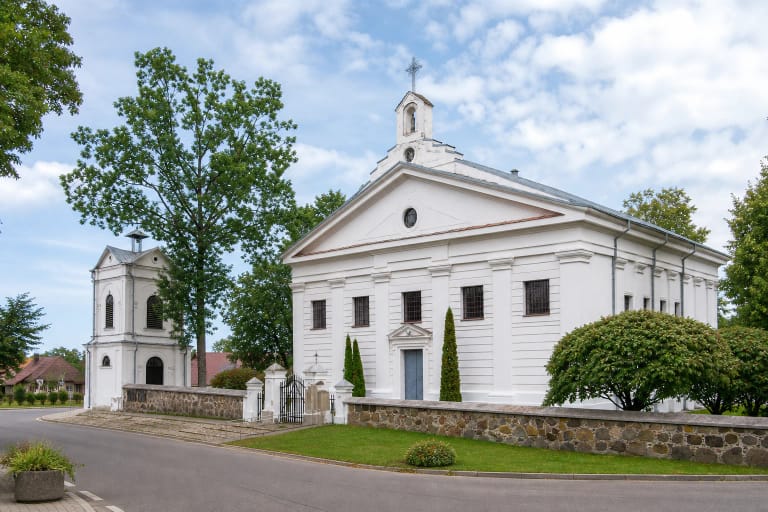 White classical facade and detached belfry of the Church of the Assumption of the Blessed Virgin Mary in Leipalingis