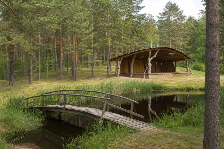 Lenkimai Forest Recreation Area pond, curved timber footbridge, and arched-roof pavilion among pine trees