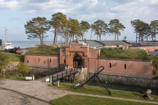 Lithuanian Sea Museum in Nerija Fort in Smiltynė, with red-brick gates, bridge, pines, and maritime exhibits