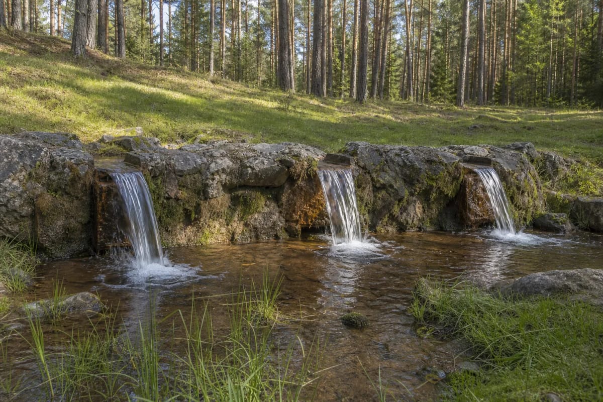 Stone retaining wall of Lino Verdenė Spring with three water spillways below a pine-covered slope