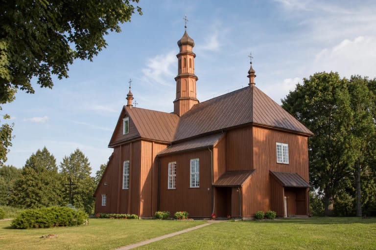 Ruda medinė Liolių bažnyčia su aukštu centriniu bokštu žaliame šventoriuje