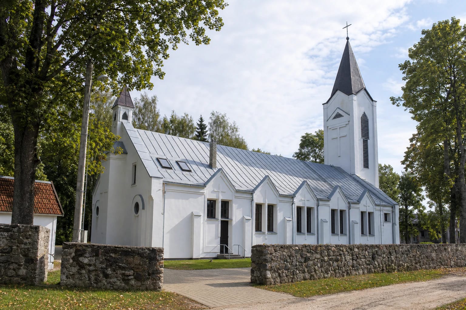 Liudvinavas St Louis Church with white façades, a grey roof, towers, and a rough-stone churchyard wall