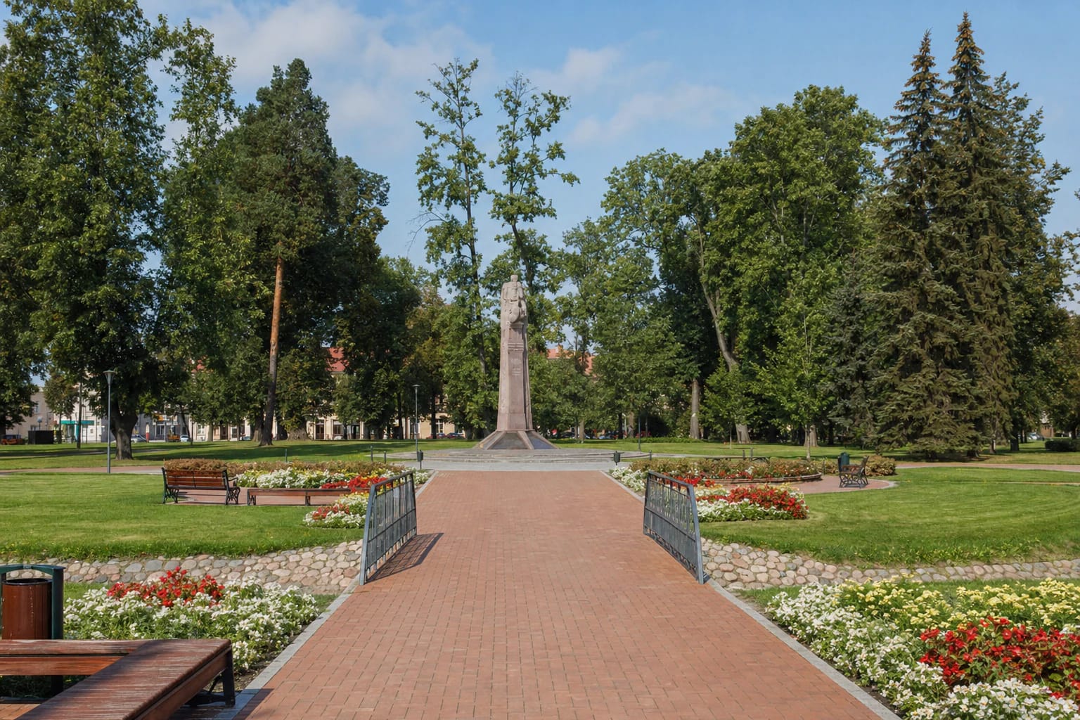 Red-brick path and bridge over the Jevonis in Vytautas the Great Park, with the equestrian monument among mature trees