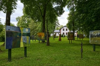 Large colourful paintings on stands across a meadow among mature trees in the Lithuania Minor Picture Garden