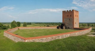Red-brick donjon and fieldstone defensive walls of Medininkai Castle with green courtyard
