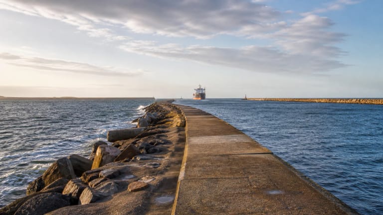 Melnragė north pier at the Klaipėda port gates with Baltic waves, pale walking surfaces, and a ship entering in the distance