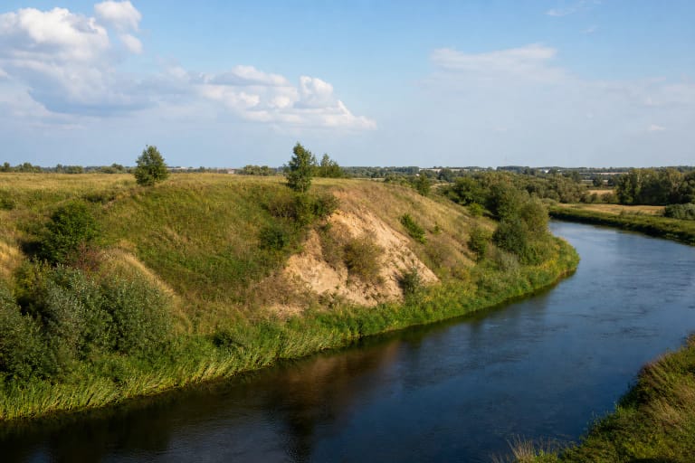 Green riverbank spur of Meškučiai Hillfort with an exposed face above the winding Šešupė in Marijampolė