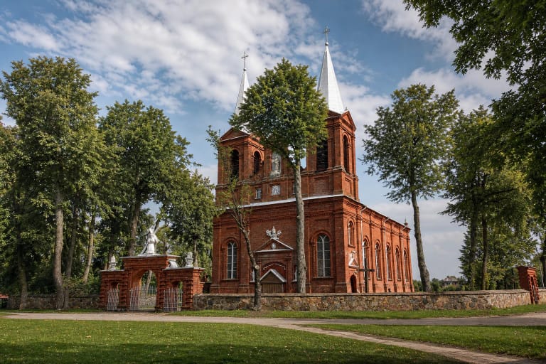 Meškuičių Šv. vyskupo Stanislovo bažnyčia su raudonų plytų fasadu, dviem šviesiais bokšteliais ir medžiais apaugusiu šventoriumi