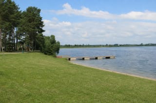 Grassy and sandy Lake Metelys bathing shore with pines, a long low pier, and an open lake horizon