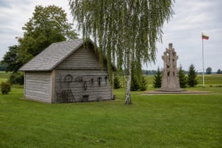 Atkurta pilka medinė klėtis virš Minaičių partizanų bunkerio ir LLKS deklaracijos memorialas kaimo sodybos kraštovaizdyje