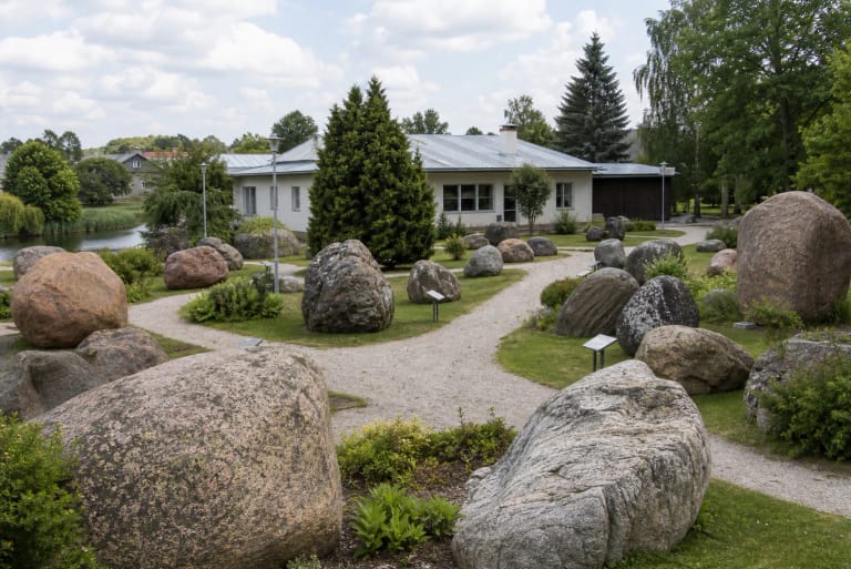 Открытая экспозиция музея камней Моседиса с большими валунами, дорожками, посадками и зданием музея