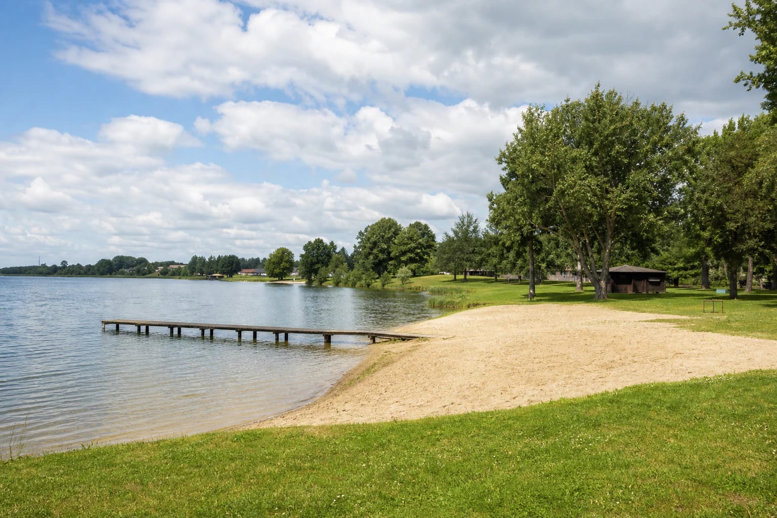 Mosėdis Beach with a sandy shore, wooden jetty, and green recreation area beside the pond