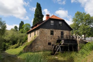 Fieldstone Mosėdis Watermill with a red tile roof beside the Bartuva and its restored wooden waterwheel