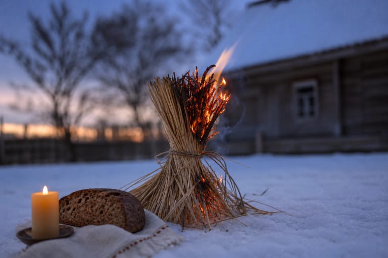 A New Year straw sheaf burning in snow beside a candle and rye bread