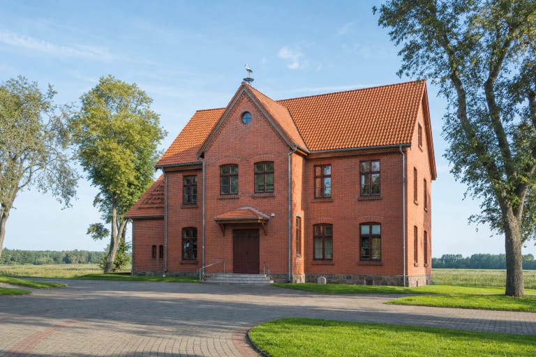 Raudonų plytų Nemuno deltos regioninio parko lankytojų centro pastatas Rusnėje su čerpiniu stogu ir grįstu kiemu