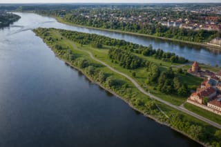Зелёный полуостров парка у слияния Немана и Нериса между двумя реками, с извилистой дорожкой, взрослыми деревьями и Каунасским замком на краю