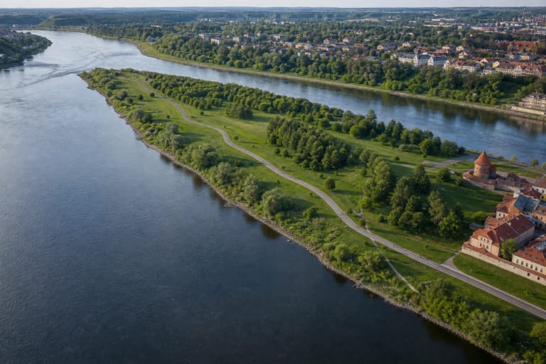 Green peninsula of Nemunas and Neris Confluence Park between two rivers, with a winding path, mature trees, and Kaunas Castle at its edge
