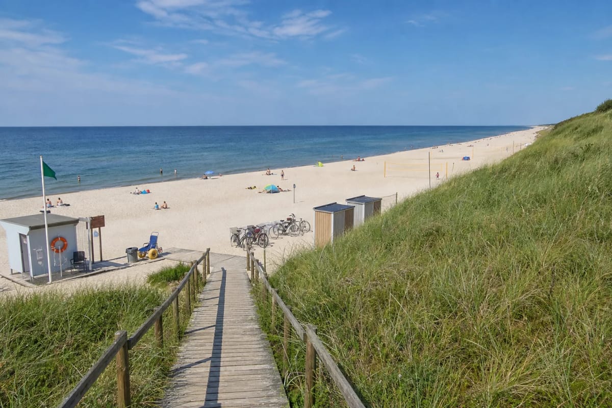Wooden boardwalk crossing a grass-covered foredune to broad white-sand Nida Central Beach on the Baltic Sea