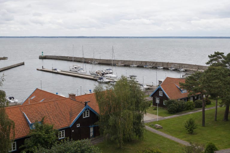Nidos uosto baseinas su jachtomis, ilgu betoniniu molu ir Kuršių mariomis, žvelgiant virš tamsių medinių Nidos namų