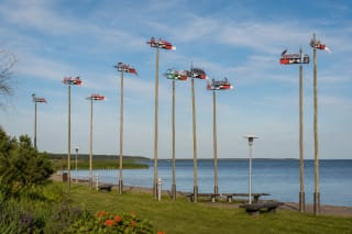 Tall wooden masts of the Nida Weathervane Display with colourful kurenas vanes beside the Curonian Lagoon