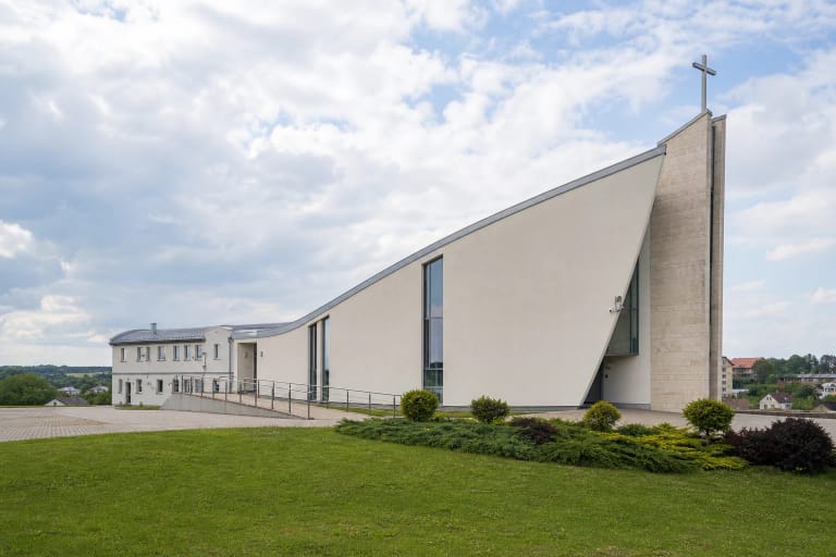 Moderni Pabradės Šeimų Karalienės bažnyčia ant žalios kalvos su išgaubtu laivo formos tūriu ir kryžiumi