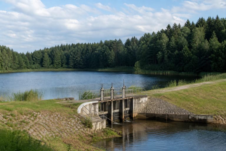 The surroundings of Pabradė Reservoir Dam beside a wooded shore and calm water