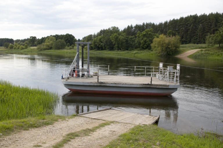 Pilkas Padalių-Čiobiškio srovinis keltas su dviem pontonais, metaliniais turėklais ir lyno rėmu plaukia per žalių krantų supamą Nerį