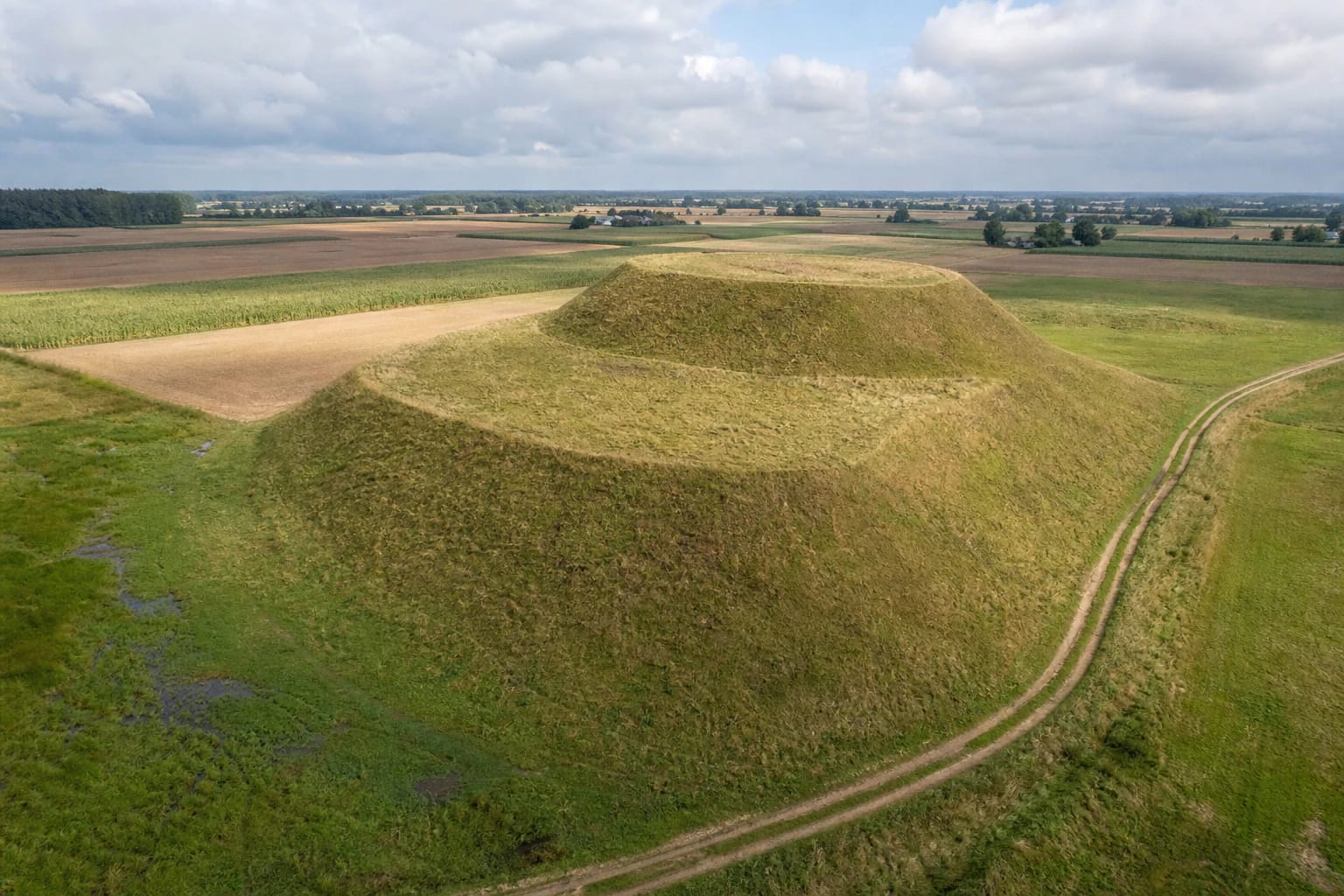 Atviras žolėtas dviejų pakopų Padovinio piliakalnis tarp plačių Sūduvos laukų