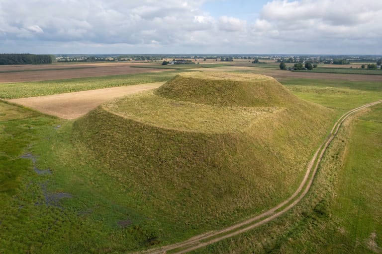 Atviras žolėtas dviejų pakopų Padovinio piliakalnis tarp plačių Sūduvos laukų