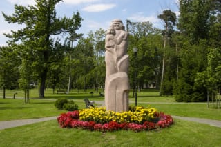 Steponas Juška's pink-granite mother-and-child monument in a flower ring within green Pagėgiai Central Park