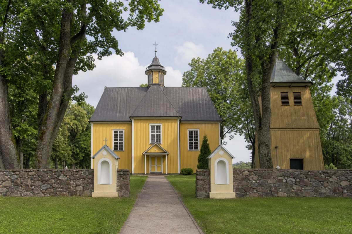 Geltona medinė Pagramančio bažnyčia, atskira varpinė ir akmenų mūro šventoriaus tvora
