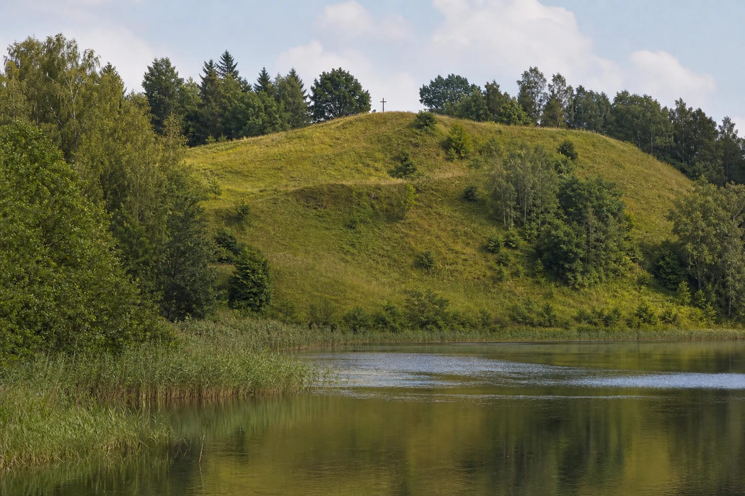 Grass-covered Pakalniai Hillfort beside Vidinkstas Lake, surrounded by deciduous woodland