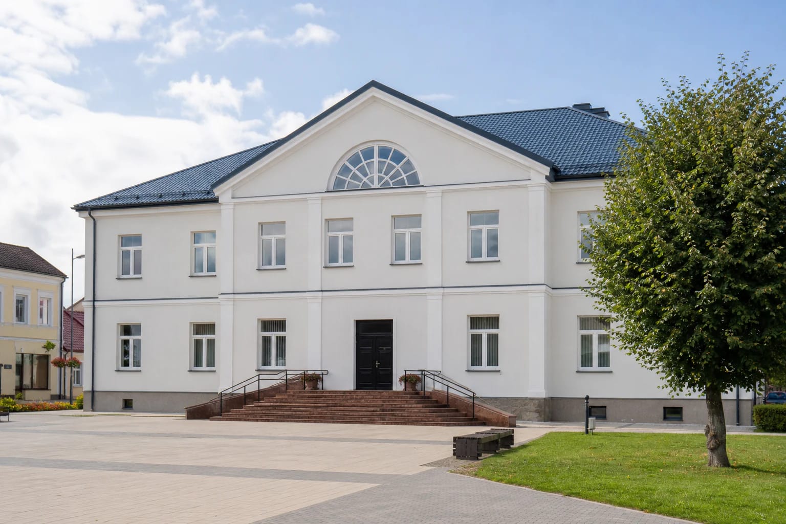 Светлое двухэтажное здание культурного центра Пакруойиса с синей крышей и широкими ступенями