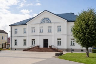 Светлое двухэтажное здание культурного центра Пакруойиса с синей крышей и широкими ступенями