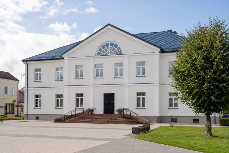 Šviesus dviejų aukštų Pakruojo kultūros centras su mėlynu stogu ir plačiais įėjimo laiptais