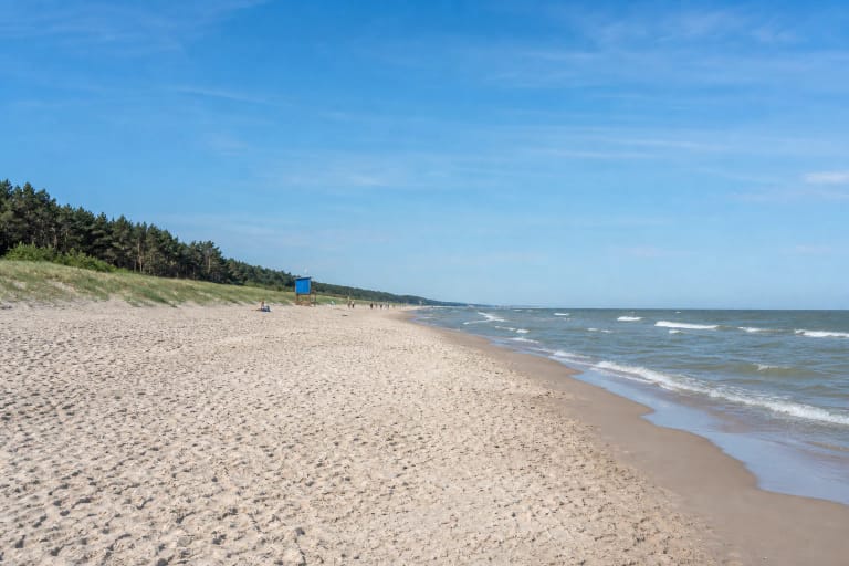 Palangos paplūdimio šviesus smėlis, Baltijos bangos, žolėmis apaugusios kopos ir mėlynas gelbėtojų postas tolumoje