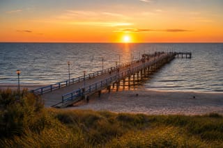 Palanga Pier stretching into the Baltic Sea with wooden walkway, railings, benches, and sunset light
