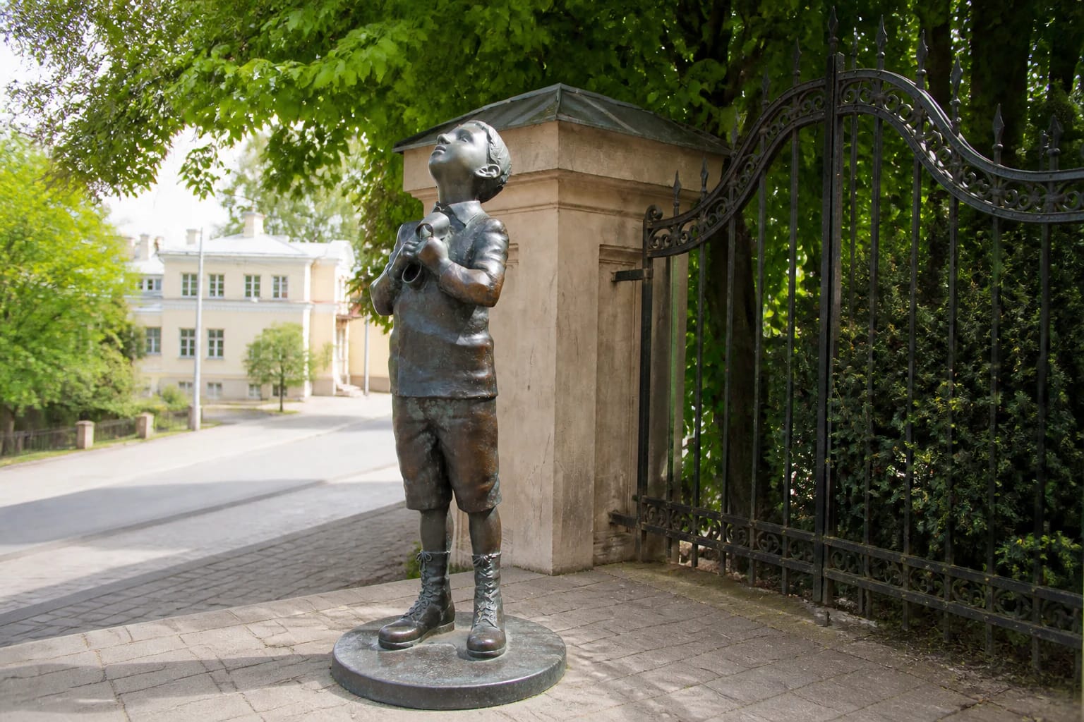 Bronze boy holding a rubber boot on a stone base beside an ornate Vilnius gate