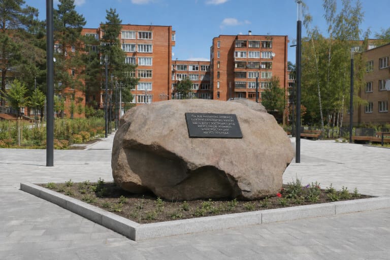 Large brown-grey Visaginas city boulder with a dark bilingual plaque in the renewed Sedulinos Avenue square