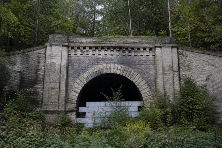Apgriuvęs šviesių plytų Panerių geležinkelio tunelio portalas miške su užtvara prieš arkinę angą