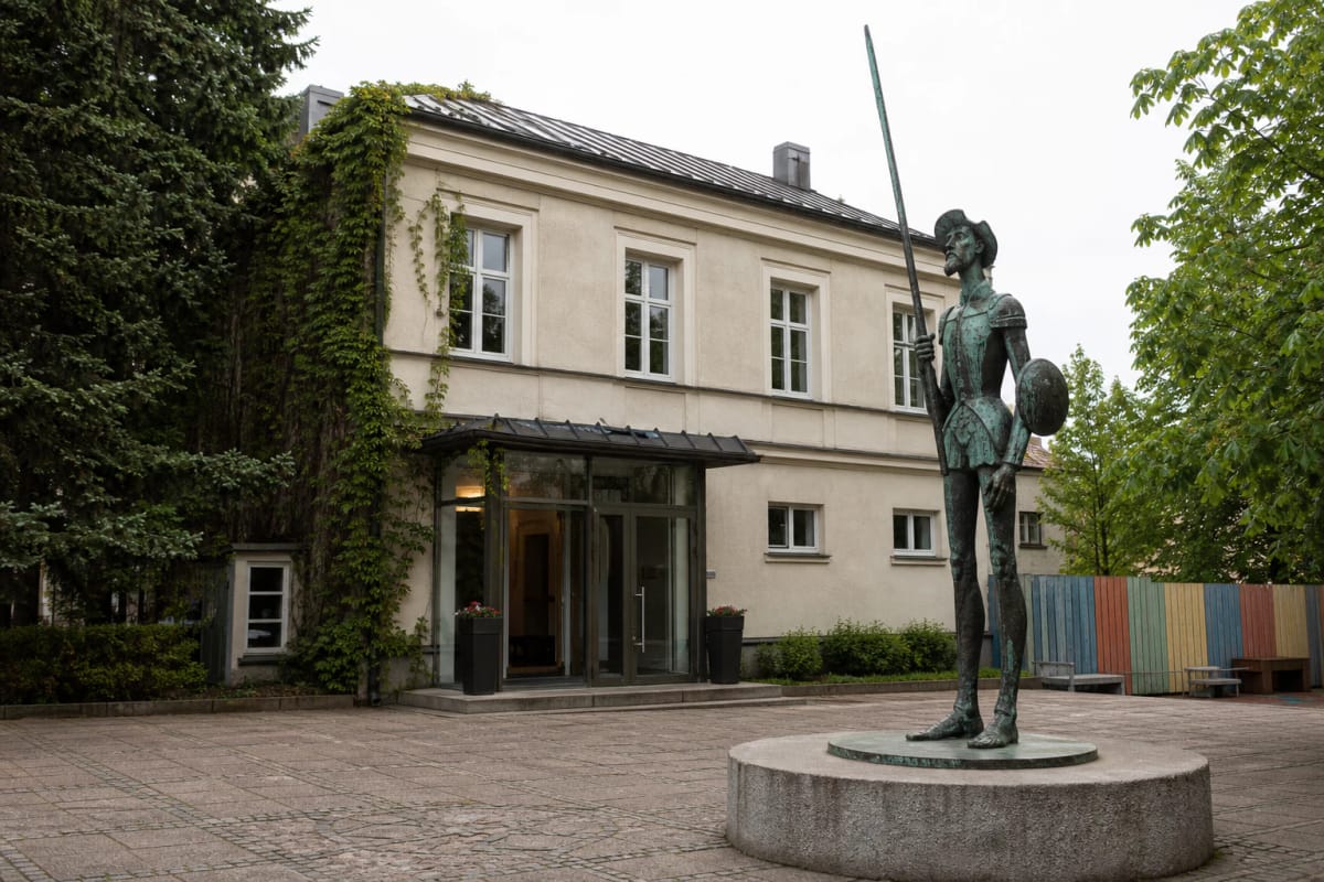 Žalvarinis Don Kichotas su ilga ietimi Panevėžio teatro „Menas“ kieme prie šviesaus istorinio pastato